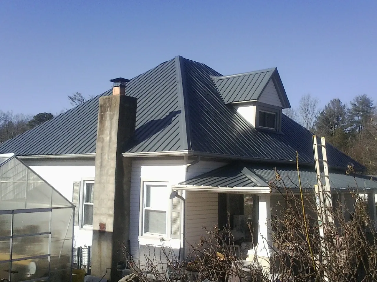 Dark blue standing seam metal roof on a white farmhouse with dormer — Slate & Tile Roof Repair by Roofing Brothers in Hohenwald