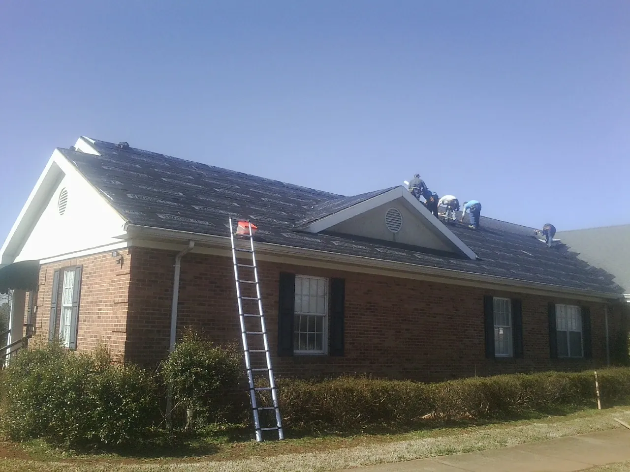 Crew tearing shingles off a brick ranch roof with a ladder set — Emergency Roof Repair work by our crew in Hohenwald