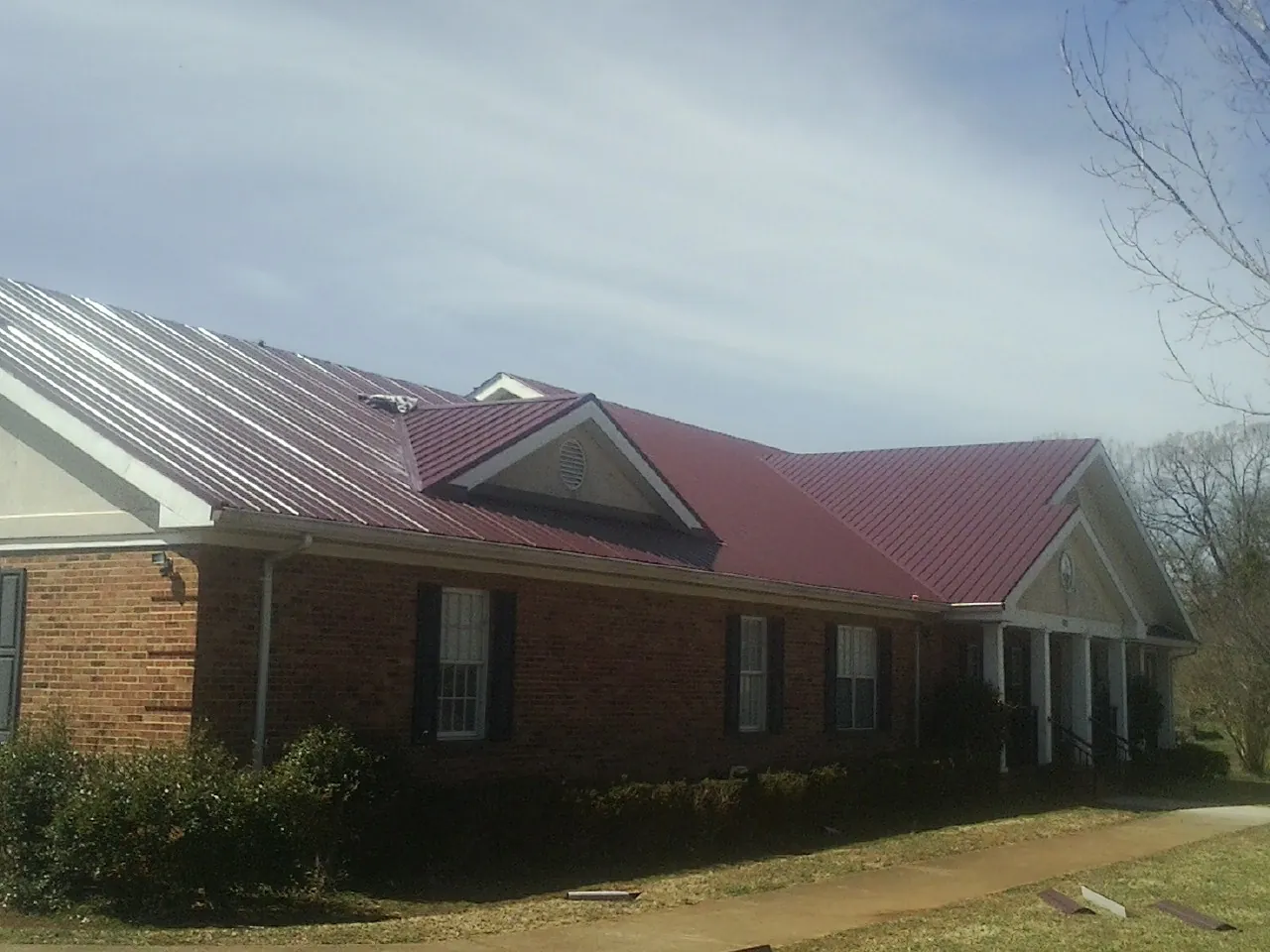 Red metal roof with gabled entries on a long brick building, from a Hail Damage Roof Repair job in Hohenwald