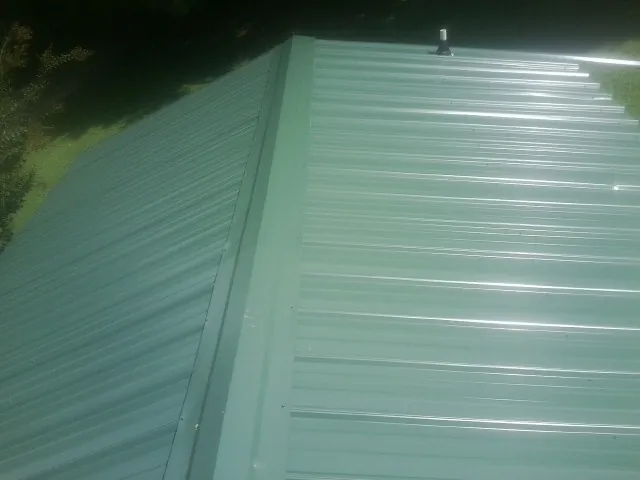 New green metal panels meeting at the ridge of a roof — Flat Roof Repair work by our crew in Hohenwald