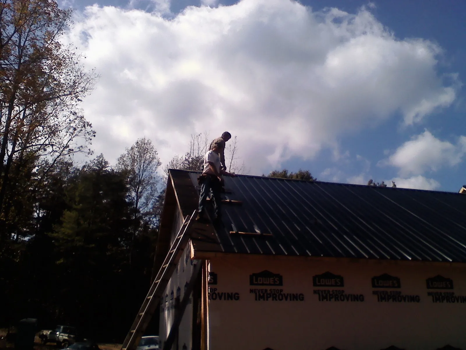 Roofer fastening dark metal panels high against a cloudy sky, from a Roof Inspection job in Hohenwald