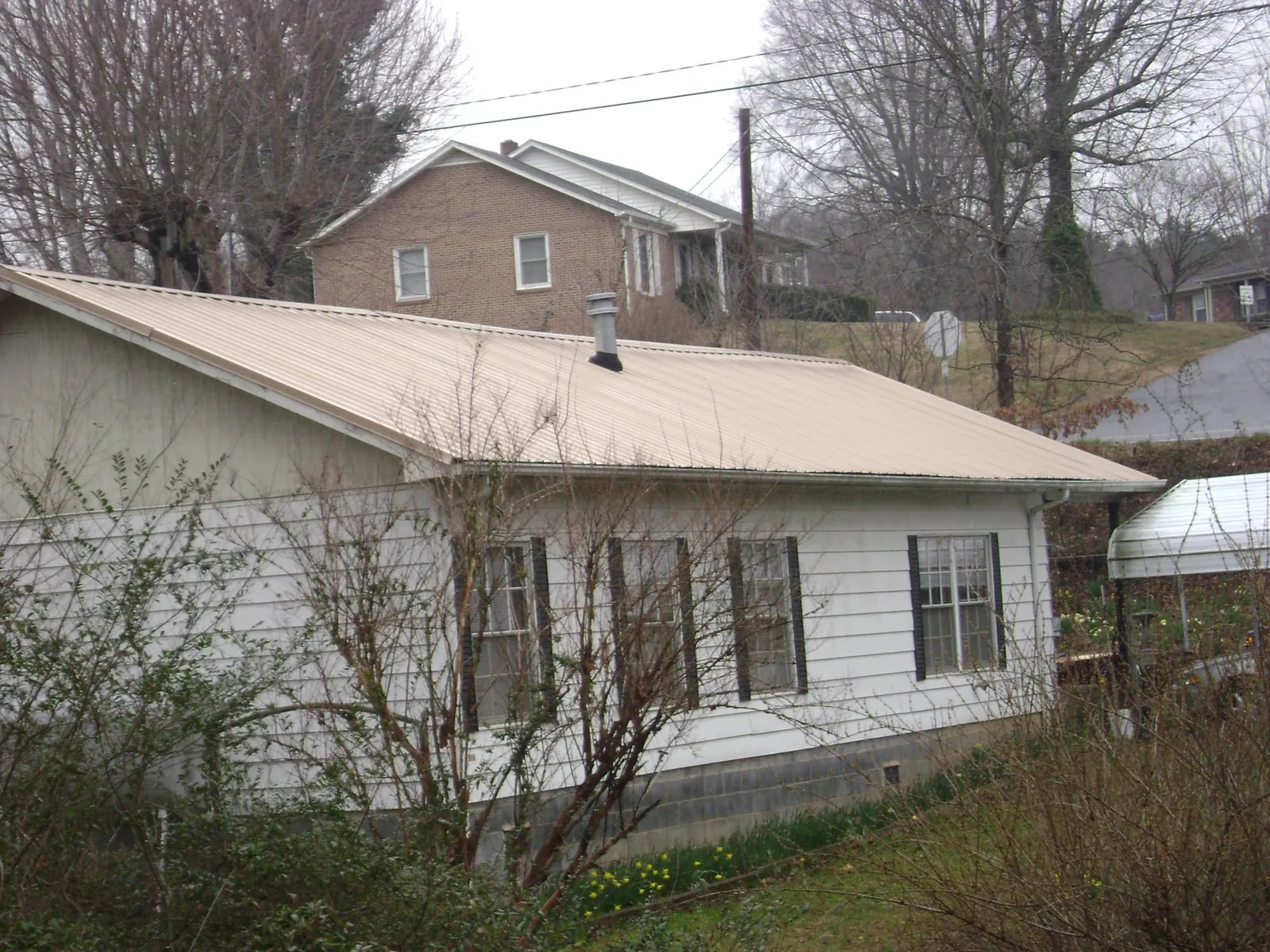 Tan metal roof on a white sided house set into a hillside — Commercial Roofing by Roofing Brothers in Hohenwald