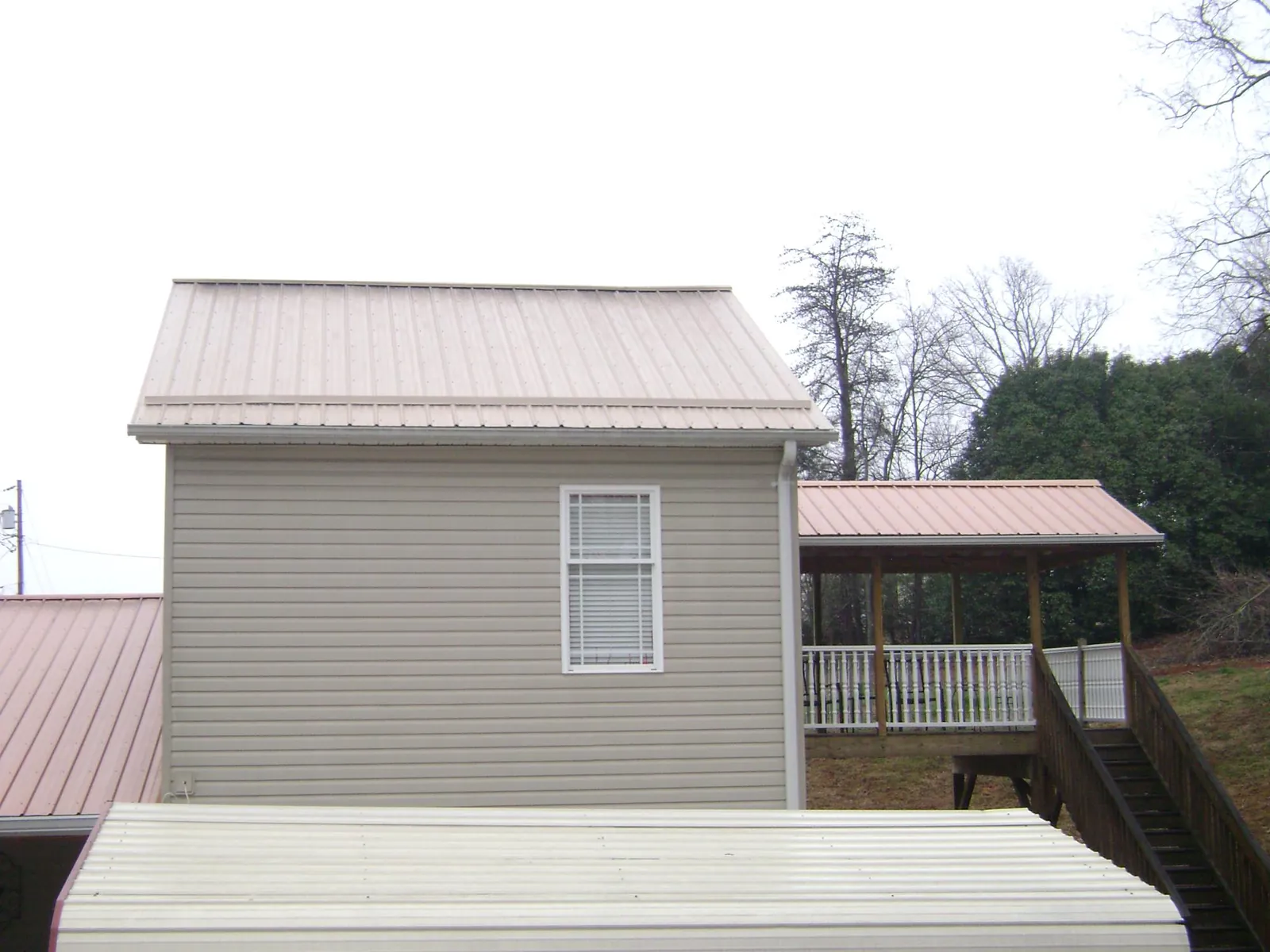 Tan metal roofs on a two story addition and attached porch, from a Roof Replacement job in Hohenwald